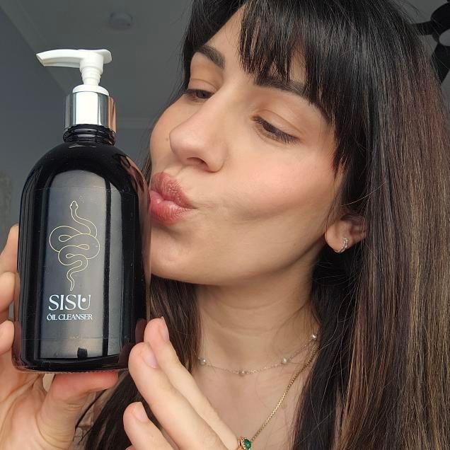 woman with glowing skin holding a large glass oil cleansing bottle that's perfect for acne prone and senstive skin. Removes water proof and long wearing makeup and removes sunscreen. it's a truly effective skin cleanser for all skin types